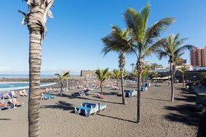 Una playa con palmeras, sillas de descanso y cielo despejado.