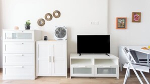A modern room with white cabinetry, a flat-screen TV, a fan, and decorative wall art.