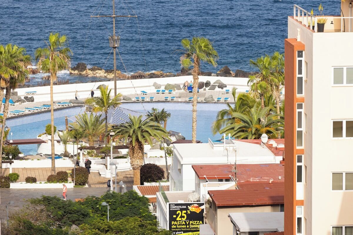Un complex turístic a la costa amb piscina, palmeres i vista al mar.