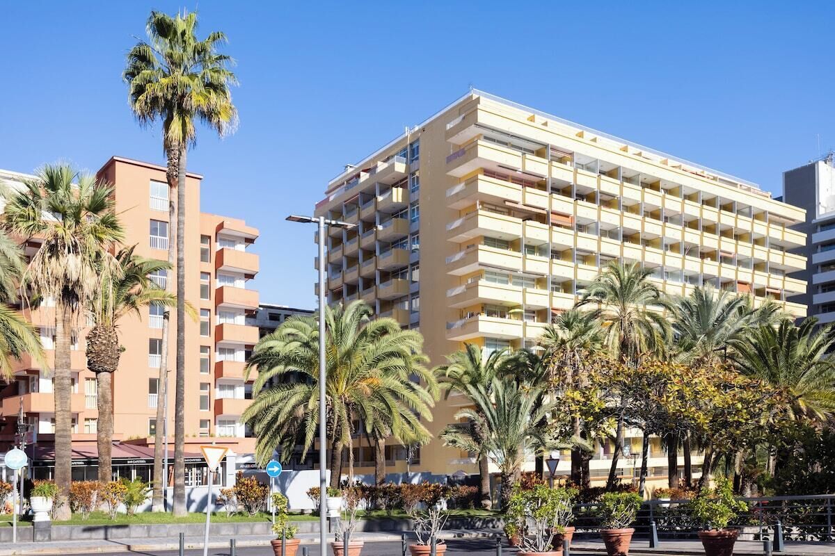 A multi-story hotel with balconies, palm trees, and a clear sky.
