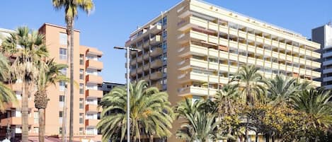 A multi-story hotel with balconies, palm trees, and a clear sky.
