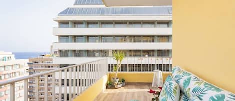 A balcony with a sofa, potted plants, and a view of a building with multiple floors.