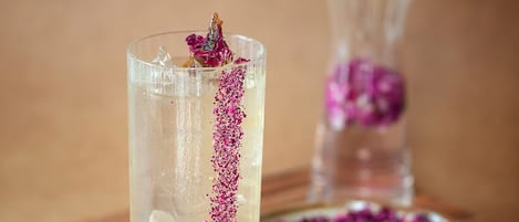A clear glass with a decorative pink garnish and a wooden tray.