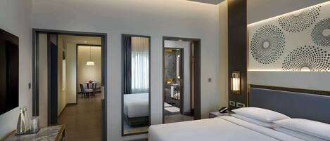 A modern hotel room with a large bed, a desk with a lamp, and a bathroom visible through an open door.