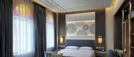 A modern hotel room with a large bed, a sofa, a desk, and a wardrobe.