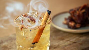 Un verre contenant une boisson claire, des glaçons et une tige de cannelle, posé sur une planche en bois.