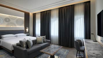 A modern hotel room with a large bed, a sofa, a coffee table, and a TV.
