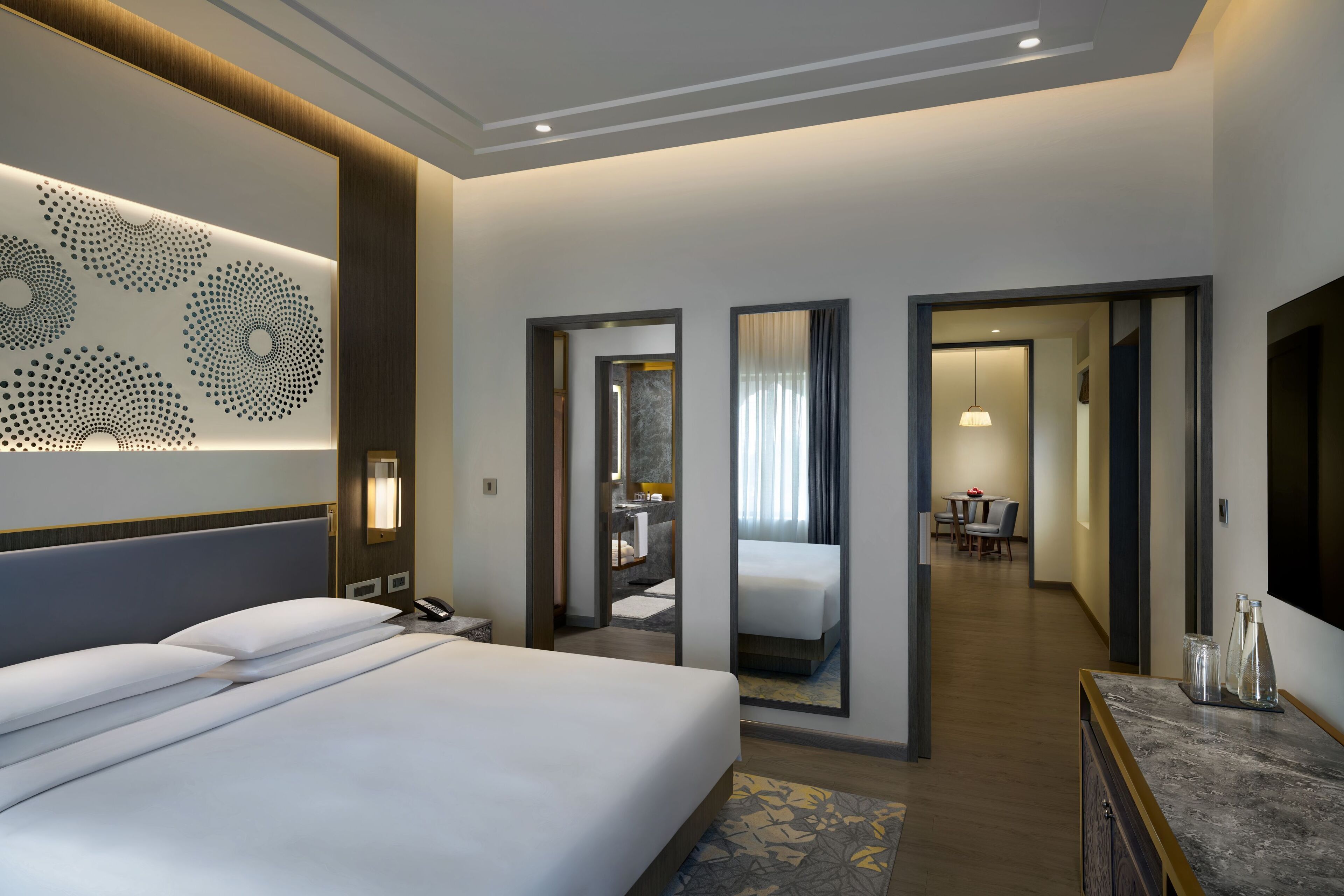 Quarto de hotel moderno com uma cama grande, uma mesa de trabalho e um banheiro visível através de uma porta aberta.