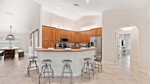 A modern kitchen with wooden cabinets, a central island with stools, stainless steel appliances, and a bright, open layout.