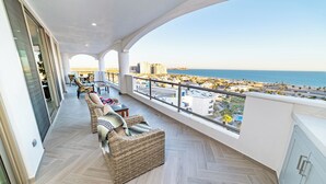 A balcony with wicker furniture, a view of the sea, and a cityscape in the background.