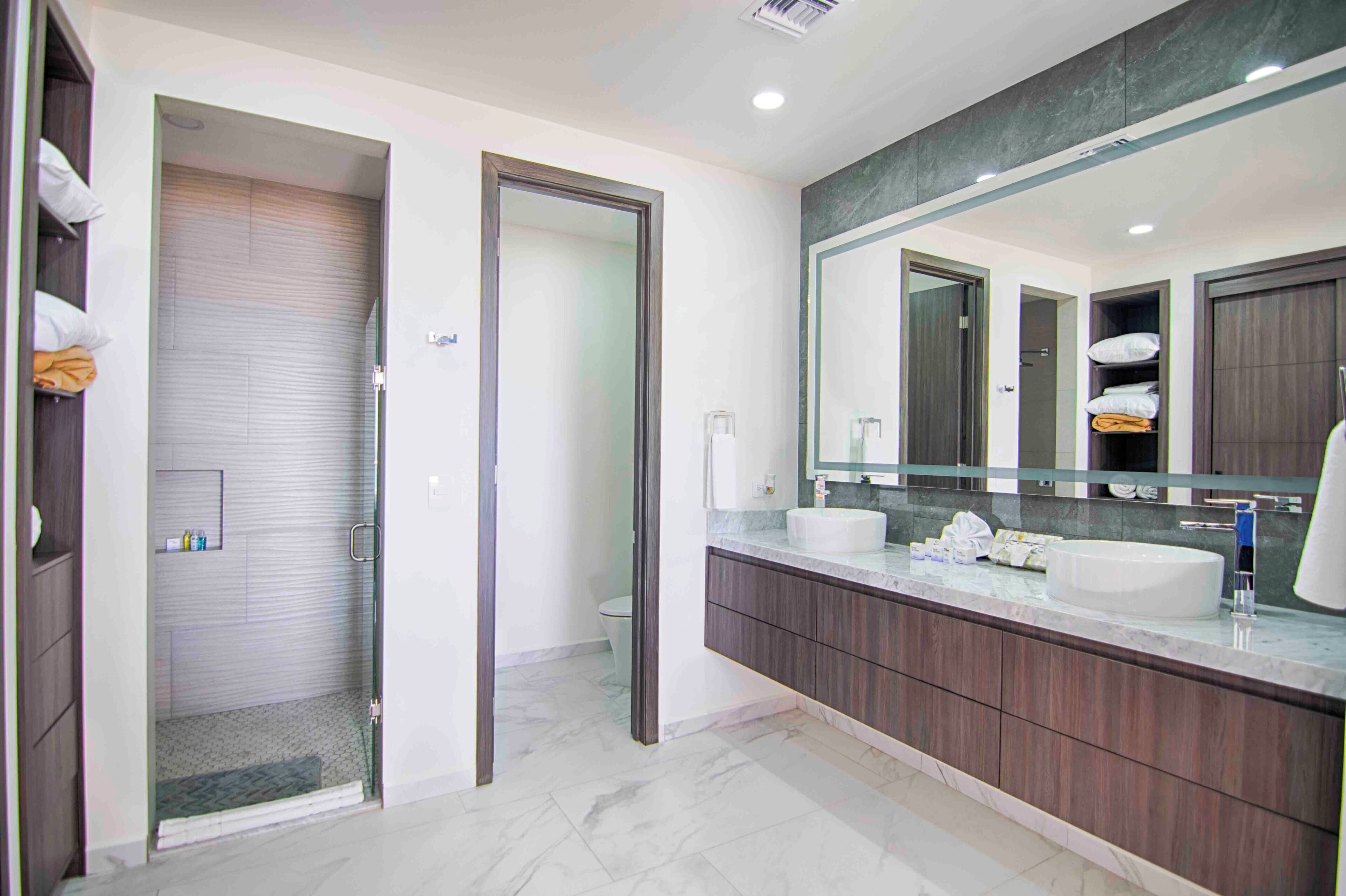 Une salle de bain moderne dotée d’une douche à l’italienne, d’un grand miroir et d’un meuble-lavabo avec un évier et un plan de travail.