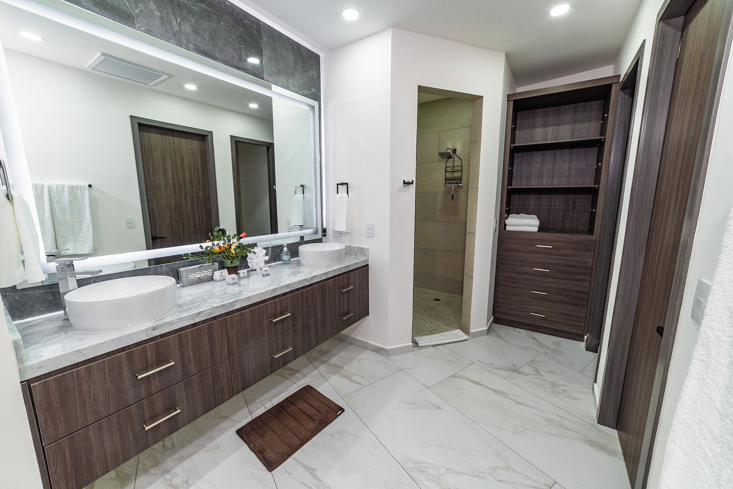 Une salle de bain moderne avec deux lavabos, un grand miroir et une douche à l’italienne.