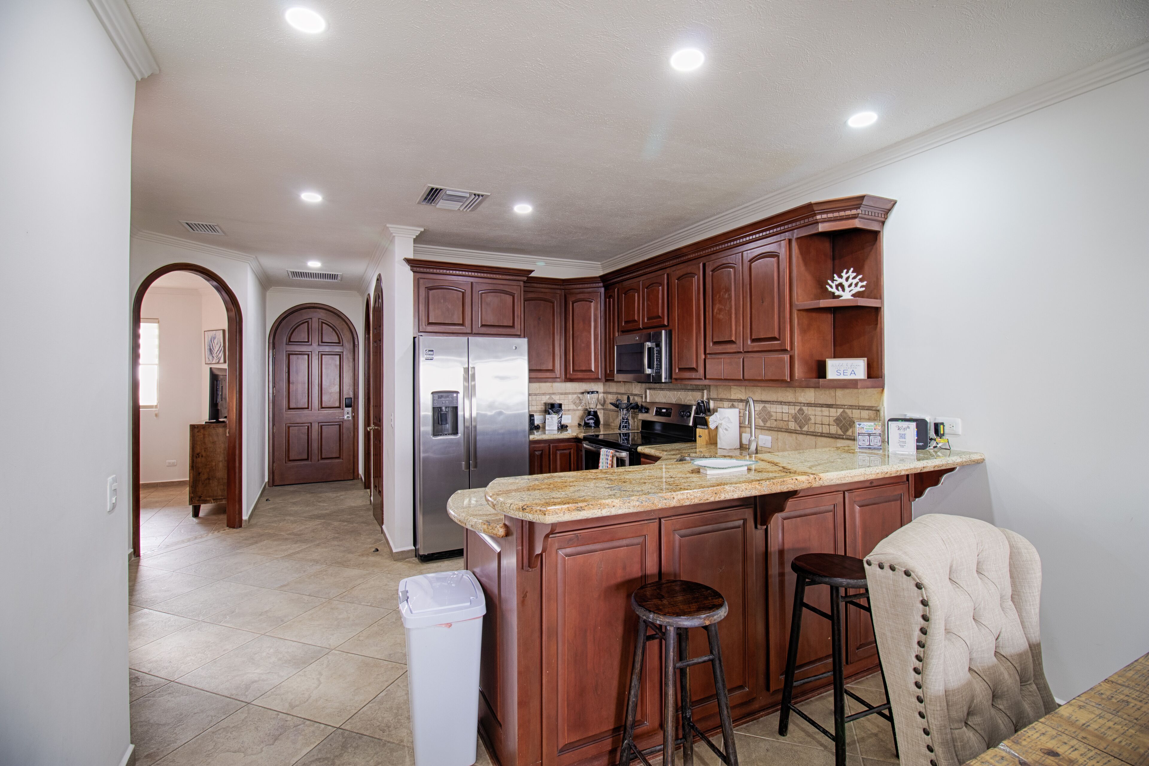 A modern kitchen with wooden cabinets, a stainless steel refrigerator, a microwave, and a granite countertop.
