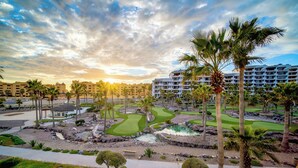 A golf course with palm trees and a hotel in the background.