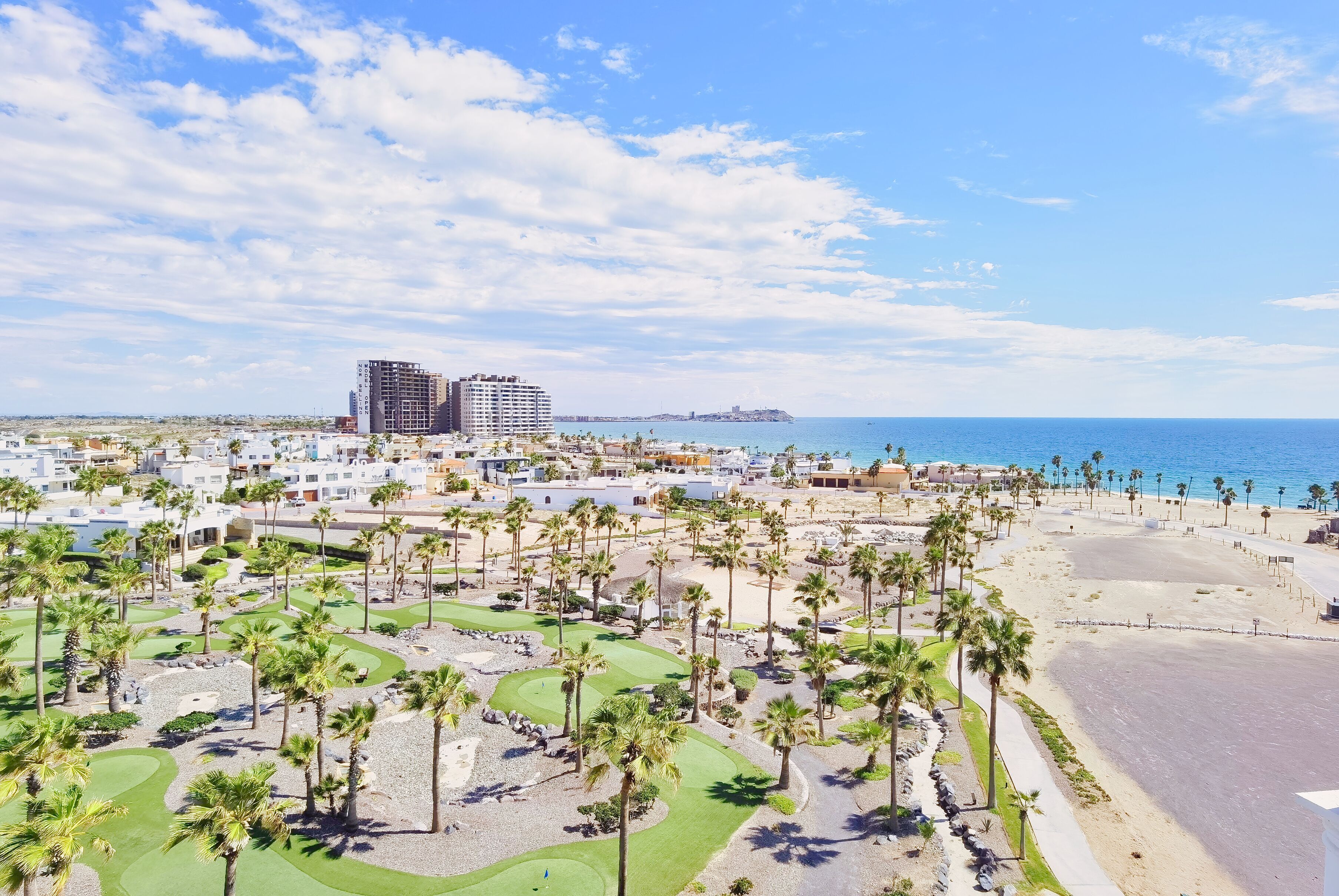 A coastal resort with a golf course, beach, and a large hotel in the background.