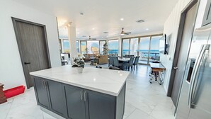 A modern kitchen with a large island, dining area with a view, and a spacious living area with a ceiling fan.