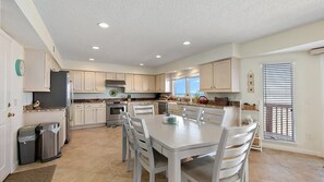 A spacious kitchen with white cabinets, a dining table, and a large window. - Steps to Sand, Pet-Friendly Oceanfront w. Dog Run (Ponte Vedra Beach)