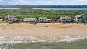 A beachfront property with multiple buildings, a sandy beach, and a view of the ocean and a forested area in the background. - Shore Beats Work Home, Deck & Oceanfront Views (Ponte Vedra Beach)