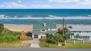 A beachfront property with a green-roofed house, a blue building, and a sandy beach. - Shore Beats Work Home, Deck & Oceanfront Views (Ponte Vedra Beach)