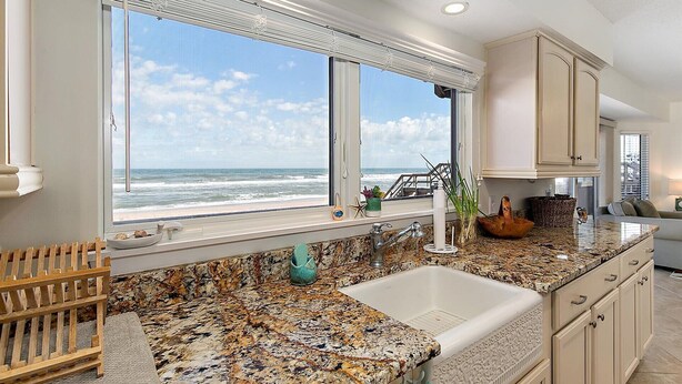 A kitchen with a large window overlooking the ocean, a granite countertop, and a sink. - Shore Beats Work Home, Deck & Oceanfront Views (Ponte Vedra Beach)