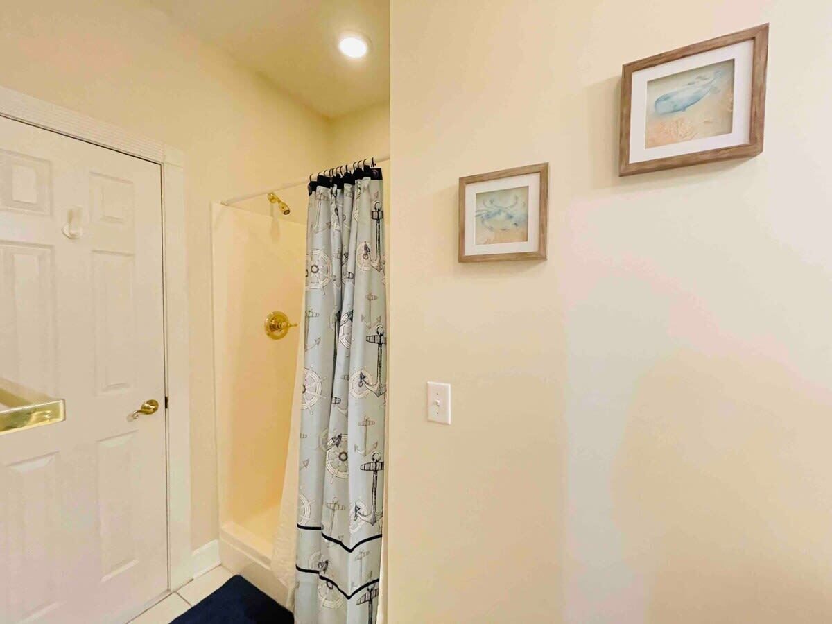 Un bagno con tenda da doccia, un quadro appeso al muro e una porta con maniglia.