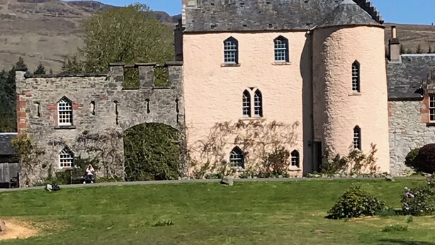 A large, historic stone building with arched windows and a reflection in a pond. - Castle Annex in Trossachs National Park (Aberfoyle)