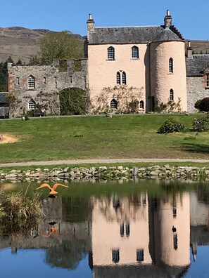 A large, historic stone building with arched windows and a reflection in a pond. - Castle Annex in Trossachs National Park (Aberfoyle)