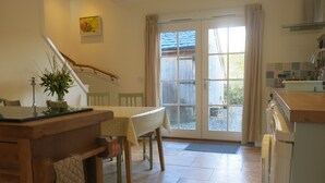 A kitchen with a wooden table, chairs, a sink, and a window with curtains. - Castle Annex in Trossachs National Park (Aberfoyle)