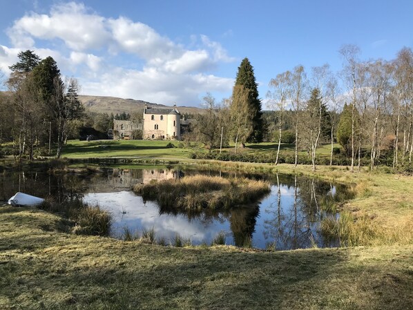 A historic stone building with a circular tower, surrounded by a pond and trees.