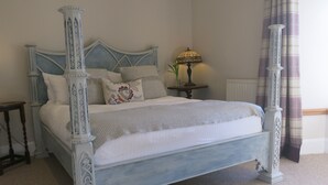 A four-poster bed with intricate designs, a bedside table with a lamp, and a window with curtains. - Castle Annex in Trossachs National Park (Aberfoyle)