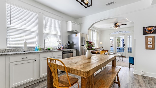 Une cuisine moderne avec des meubles blancs, une table à manger en bois et un ventilateur de plafond.