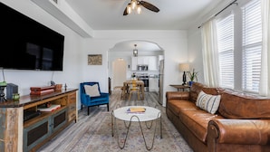Un salon avec un canapé en cuir marron, un fauteuil bleu, une table basse ronde et un téléviseur à écran plat.