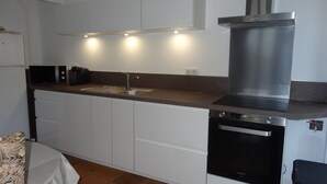 Een kleine keuken met witte kasten, een roestvrijstalen afzuigkap, een ingebouwde vaatwasser en een magnetron.