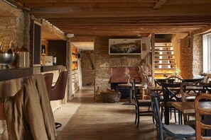 A rustic interior with exposed wooden beams, stone walls, a fireplace, and a dining area with wooden furniture. - The Crown of Crucis (Cirencester)
