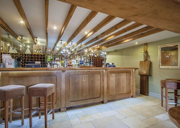 A bar area with wooden bar stools, a well-stocked liquor shelf, and a wooden ceiling. - The Crown of Crucis Country Inn And Hotel (Cirencester)