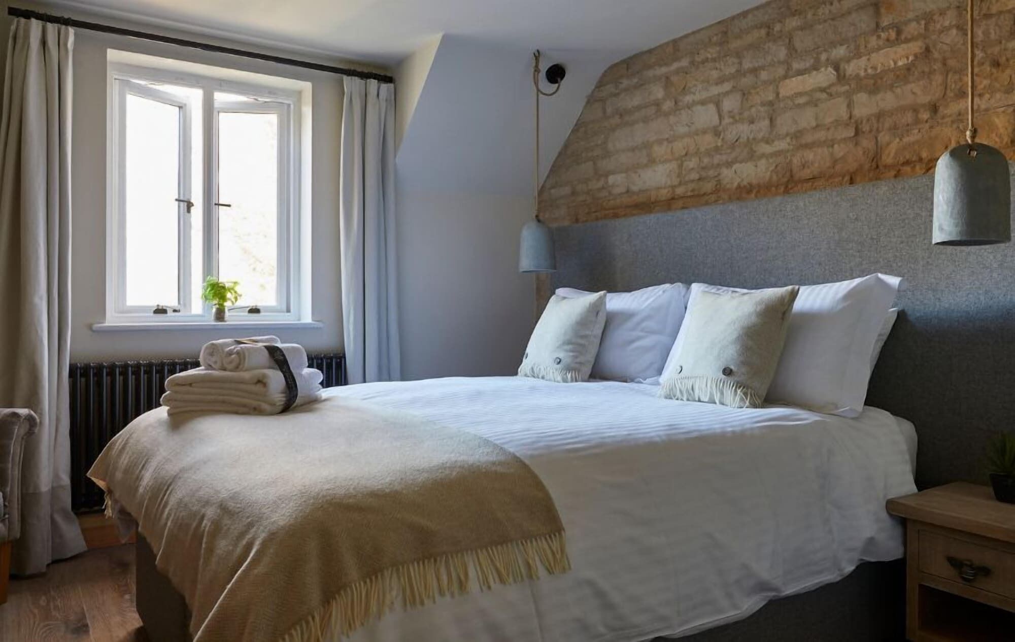 Ein ordentlich bezogenes Bett mit weißer Bettdecke und Kissen, eine Nachttischlampe, ein Fenster mit Vorhängen und eine Heizung.