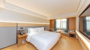 A modern hotel room with a large bed, bedside tables, a nightstand, a window with curtains, and a view of the outdoors.