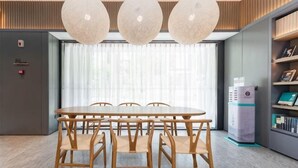 A modern dining area with a long wooden table and chairs, a large window with sheer curtains, and a water dispenser.