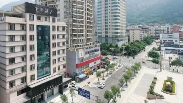 A multi-story hotel with a modern design, located in an urban area with a view of mountains in the background.