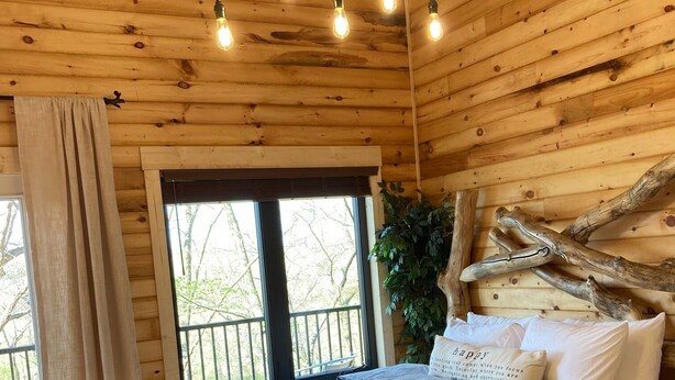 A wooden cabin bedroom with a bed, curtains, and a window.