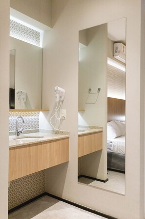 Baño de hotel con lavamanos, espejo, secador de pelo y toallero.