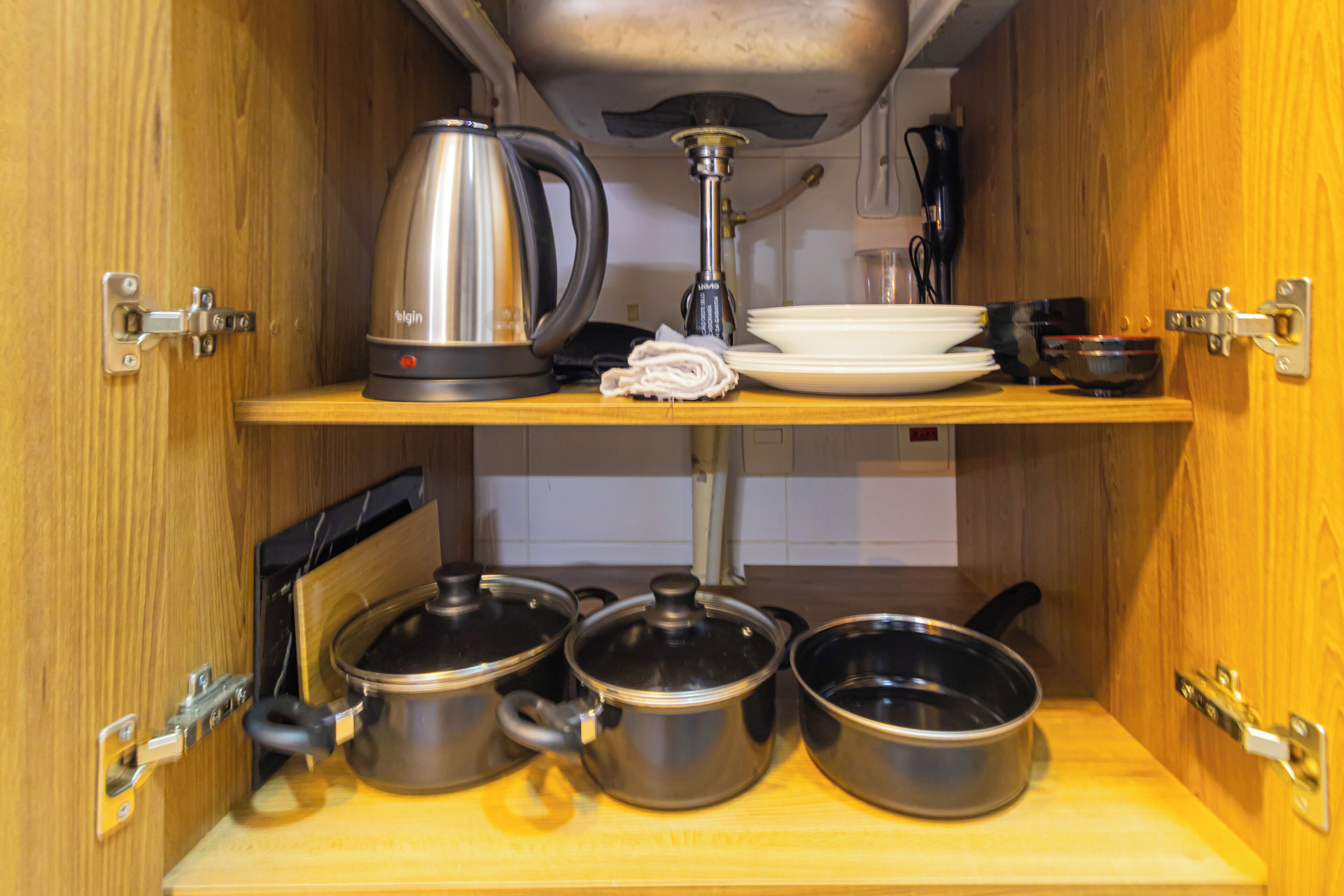 Un armario de cocina con ollas de acero inoxidable, una tetera y una cafetera.