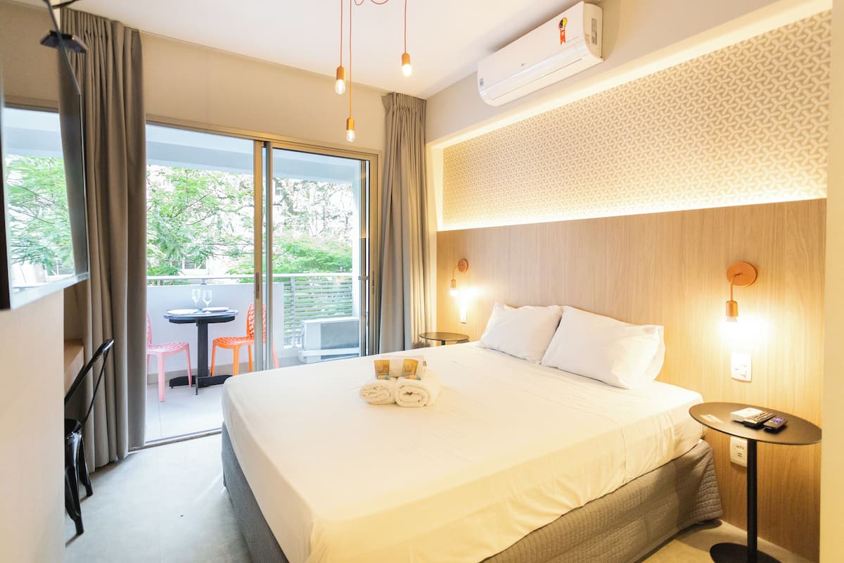 Ein Hotelzimmer mit einem großen Bett, einem kleinen Tisch, einem Sessel und einem Balkon mit Tisch und Stühlen.