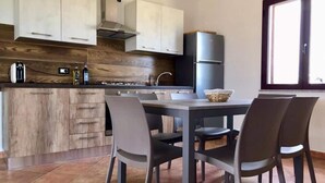 Eine moderne Küche mit Holzschränken, einem Gasherd und einem Kühlschrank. Ein Esstisch mit Stühlen und ein Fenster sorgen für natürliches Licht.