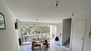 A spacious room with a large window, a wooden table with chairs, and a staircase leading to an upper level. - Donna Alda Tower incredible views (Salta)