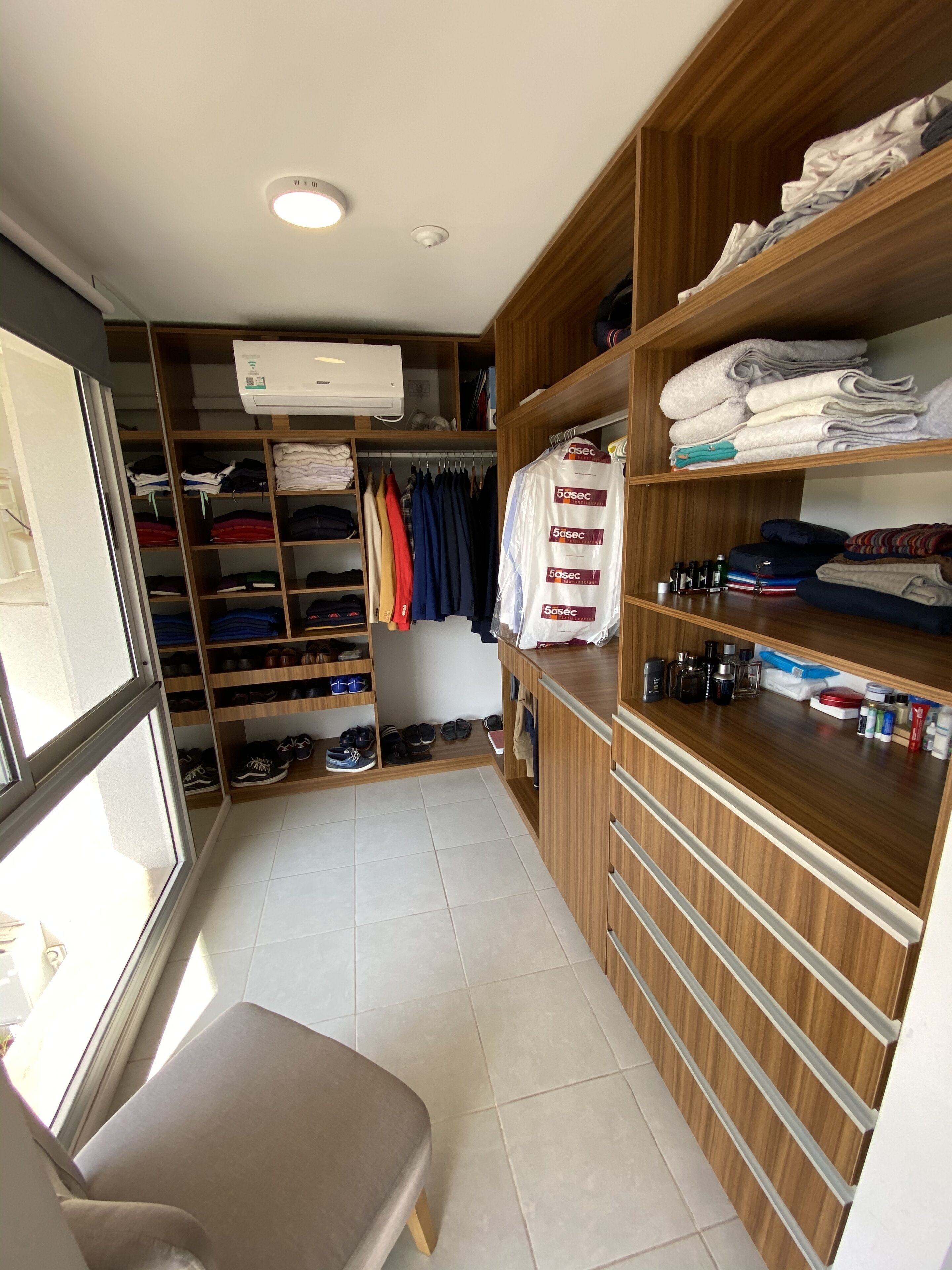 A walk-in closet with shelves, a bench, and a variety of folded clothes and shoes.