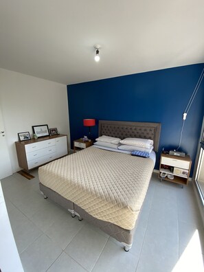 A bedroom with a bed, a dresser, a nightstand, a lamp, and a window.