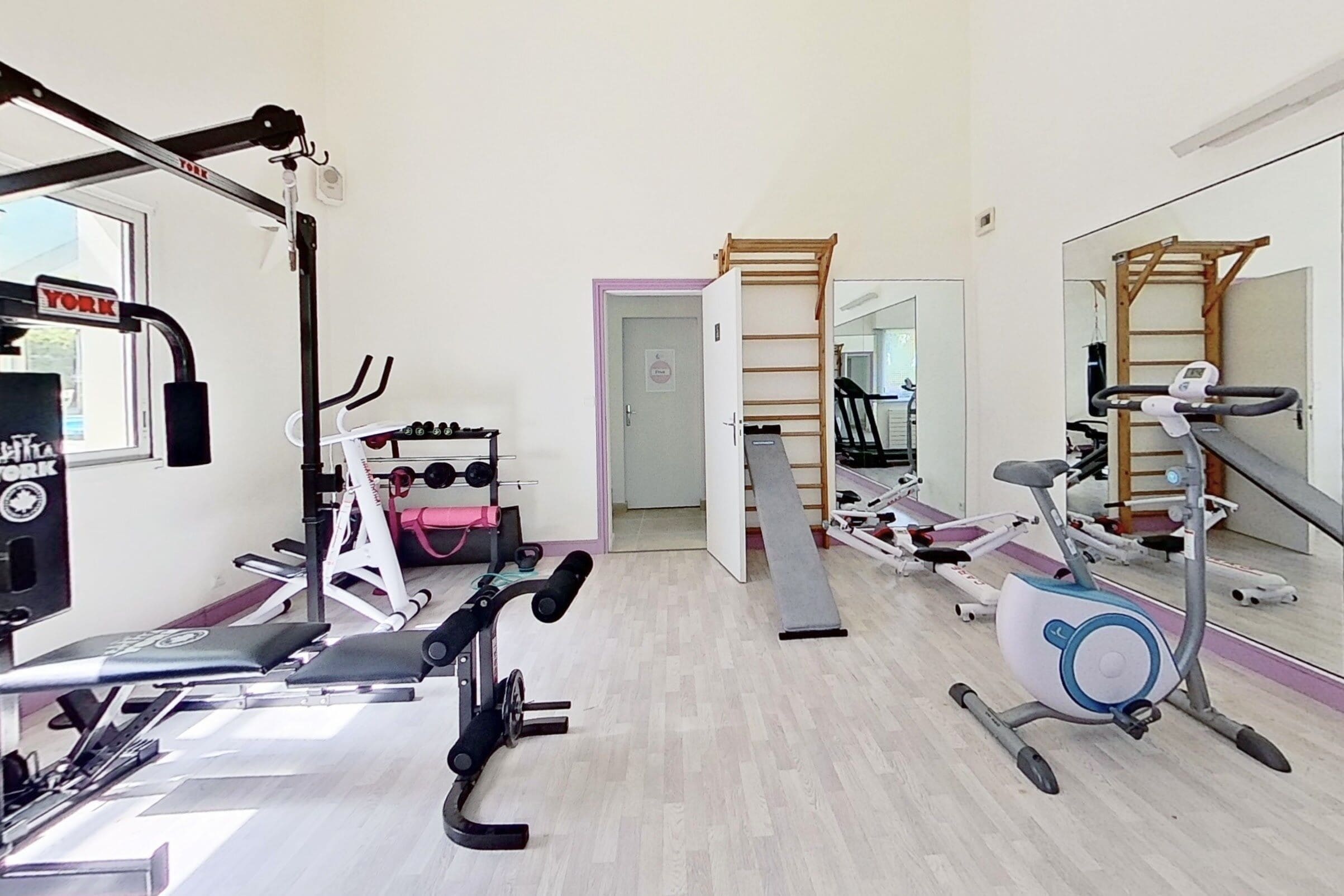 Un gimnasio con diversos equipos de ejercicio, como cintas de correr, bicicletas estáticas y máquinas de pesas.