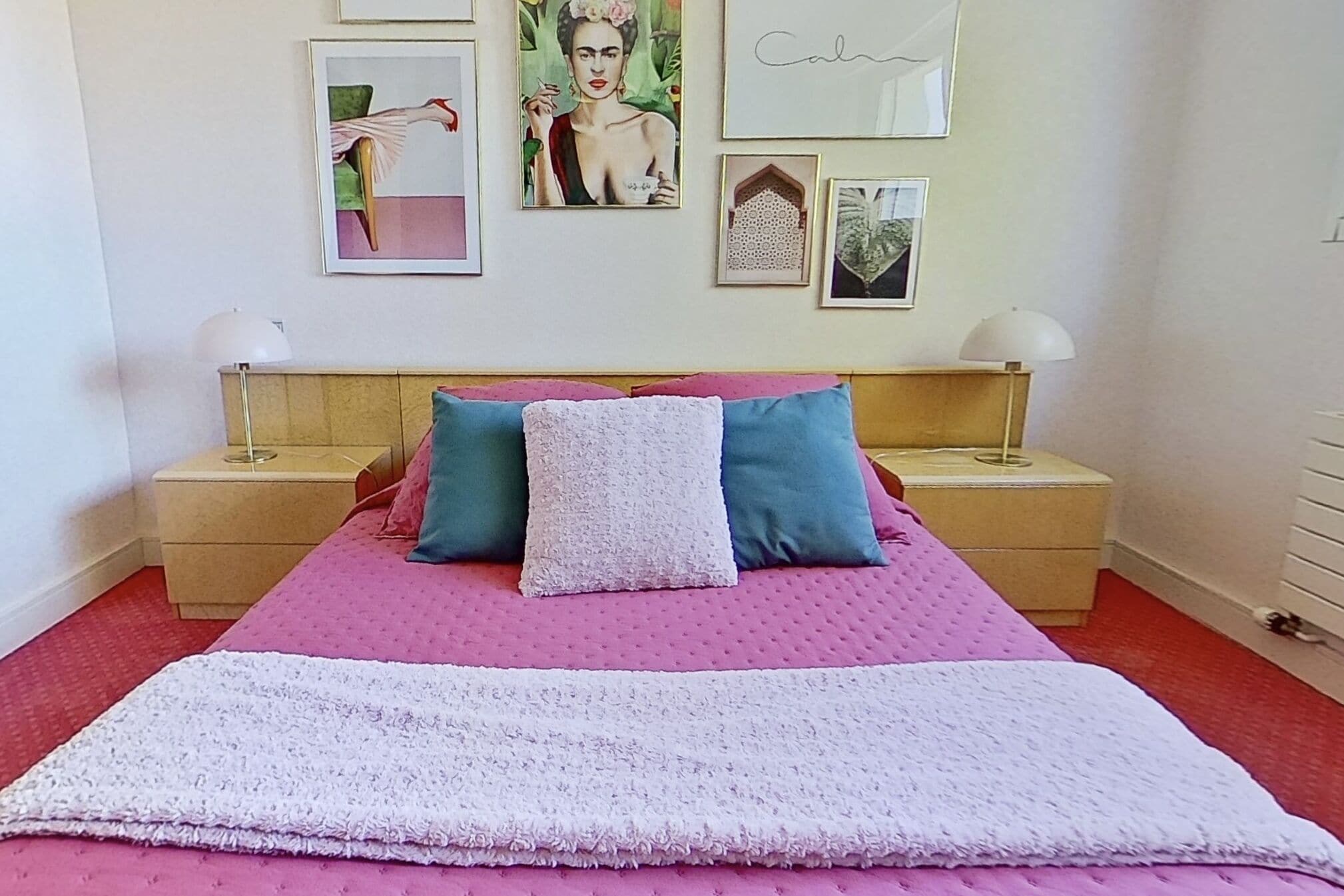 A bedroom with a pink bedspread, two pillows, a white throw blanket, and a wooden headboard.