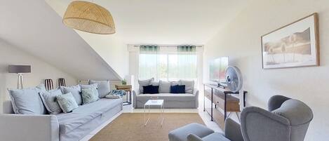 A modern living room with a grey sofa, a grey armchair, a small white table, and a large window with sheer curtains.